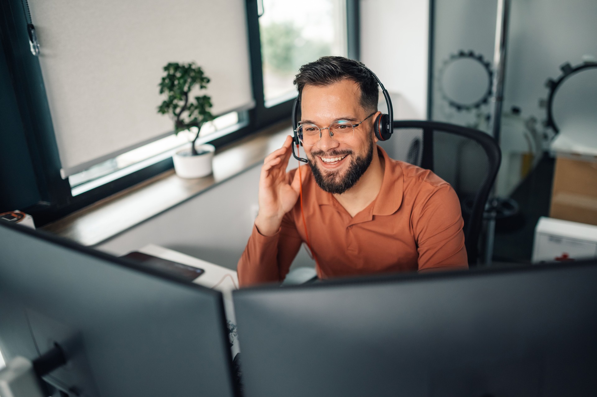 Smiling customer service representative working from home office using headset and dual monitors