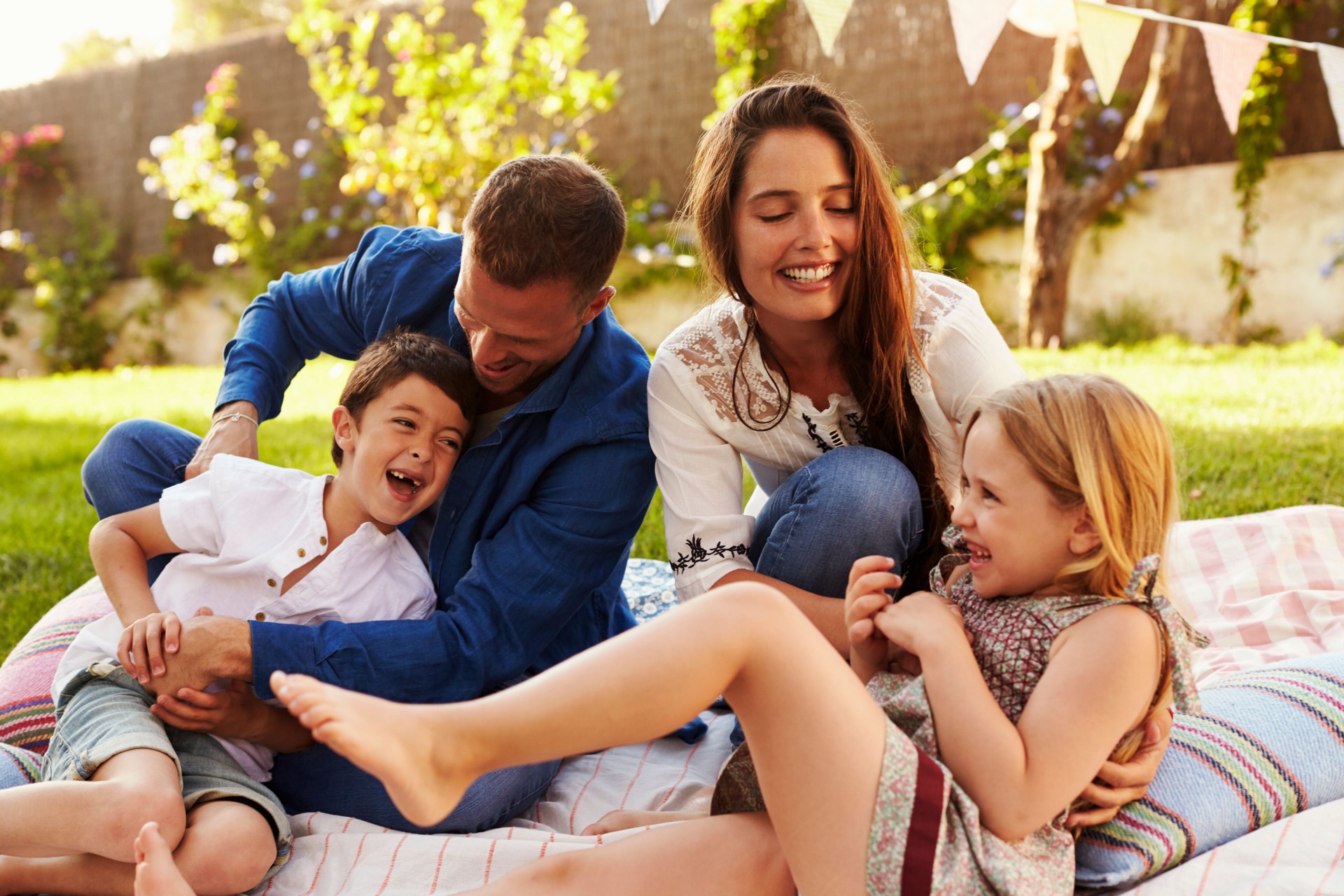 Parents Playing Game With Children On Blanket In Garden